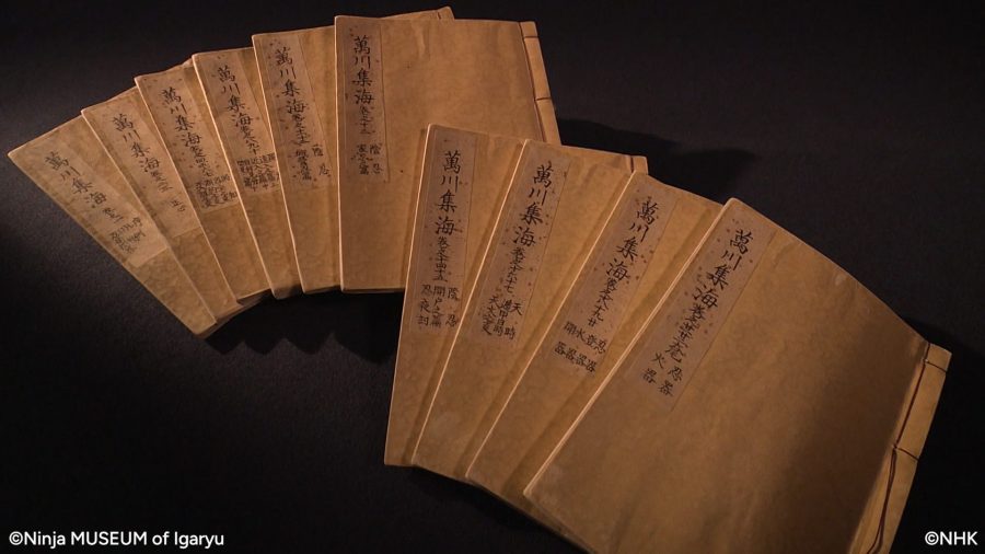 "Bansenshukai," a collection of secret ninja manuals from the Edo period. Several volumes of old, hand-bound books with brown covers are arranged in a fan shape on a black background.