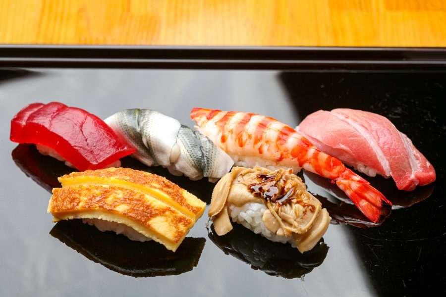 Close-up of Edomae nigiri sushi arranged on a black lacquer plate, featuring tuna, gizzard shad, shrimp, and egg.