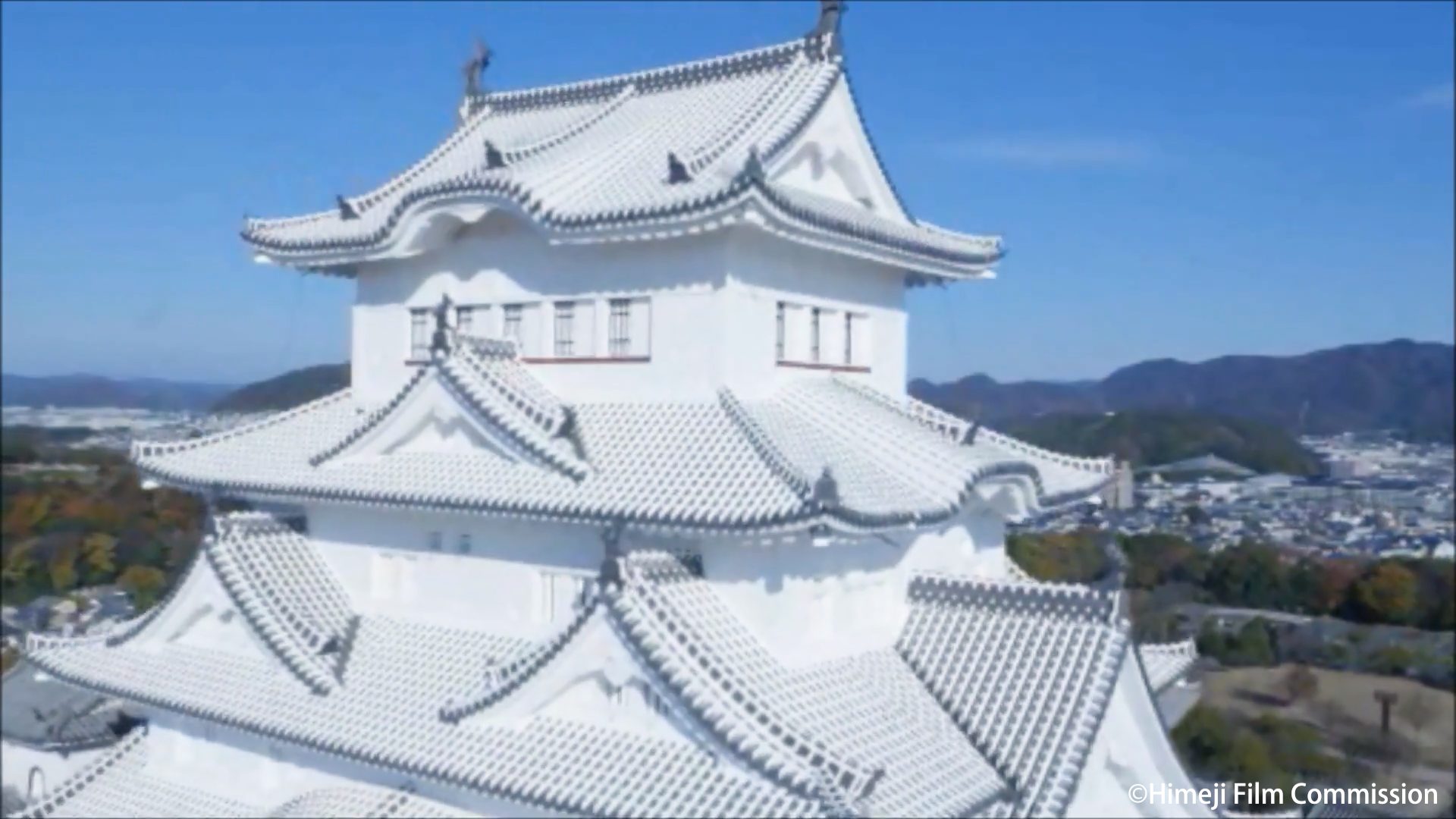 Aerial close-up of the white main keep of Himeji Castle against a blue sky.