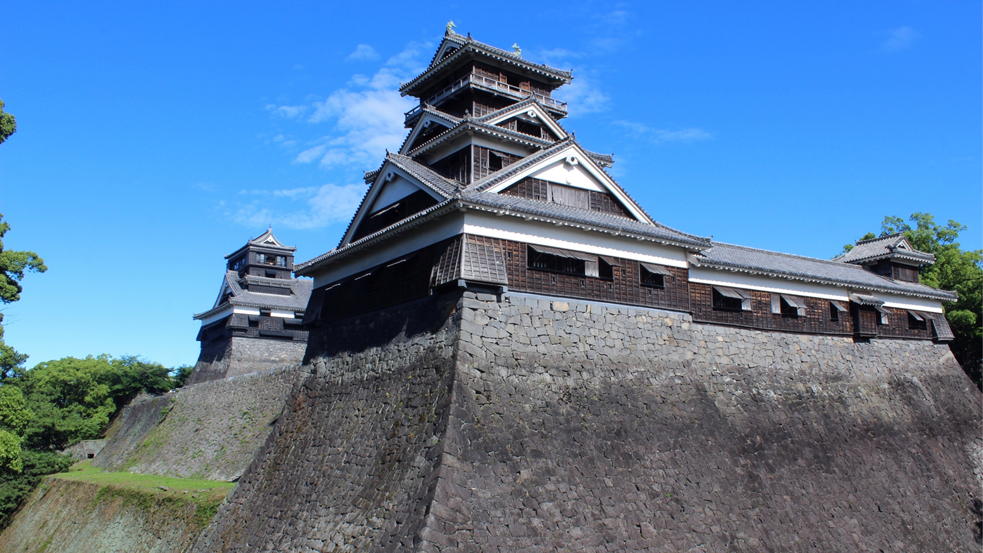 Low-angle view of Kumamoto Castle featuring its massive curved stone walls and black main keep.